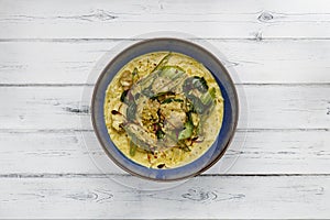 A delicious bowl of  thai chicken laxa curry,  in a dark blue bowl shot on a distressed white wooden background