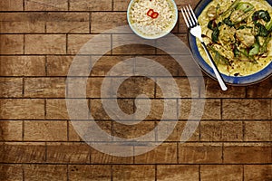 A delicious bowl of  thai chicken laxa curry,  in a rustic blue bowl with a side bowl of rice, shot on a checked wooden table top