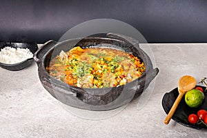 Delicious Brazilian fish moqueca with tomato, onion, olive oil, coriander and orocum seed. Made in clay pot on white table and