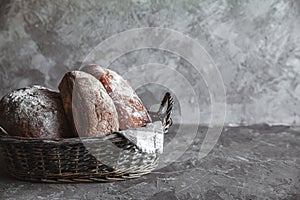 Delicious bread in basket on wooden table on gray background