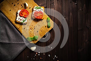 Delicious bread with cream cheese, tomato and basilico on wooden table, flat lay. Copyspace