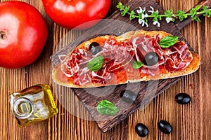 Delicious bread toast with natural tomato, extra virgin olive oil, Iberian ham, black olives and basil leaves.