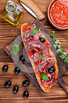 Delicious bread toast with natural tomato, extra virgin olive oil, Iberian ham, black olives and basil leaves.