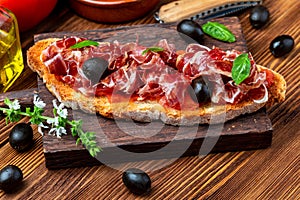 Delicious bread toast with natural tomato, extra virgin olive oil, Iberian ham, black olives and basil leaves.