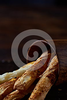 Delicious breadsticks grissini on wooden dark background in wooden oldstyle cup, close-up, selective focus