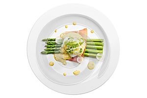 Delicious breakfast asparagus with poached egg, bacon, hollandaise sauce in a white plate. Isolated on white background. View from