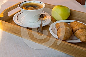 Delicious Breakfast on the balcony in the sunlight, with coffee, croissants, Apple on a wooden tray