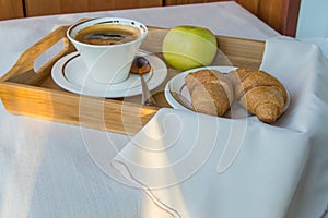 Delicious Breakfast on the balcony in the sunlight, with coffee, croissants, Apple on a wooden tray