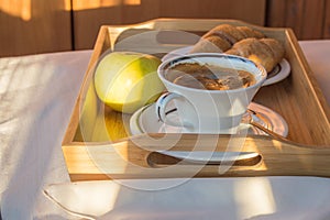 Delicious Breakfast on the balcony in the sunlight, with coffee, croissants, Apple on a wooden tray