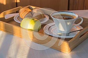 Delicious Breakfast on the balcony in the sunlight, with coffee, croissants, Apple on a wooden tray