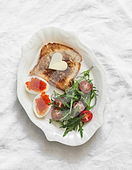 Delicious breakfast, brunch - toasts with butter, boiled eggs with red caviar, fresh salad on a light background, top view