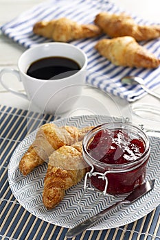Delicious breakfast consisting of croissants, jam in a jar on a plate and black coffee