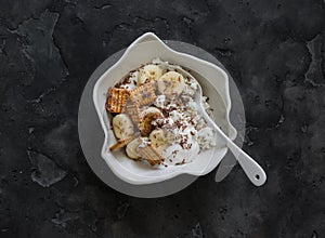 Delicious breakfast - cottage cheese with greek yogurt, banana, crackers and chocolate on a dark background, top view