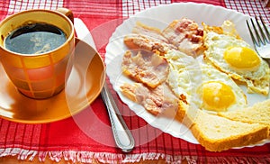 Delicious Breakfast - a Cup of coffee, a plate of fried eggs, bacon and toast, next to the Cutlery on red checkered napkin