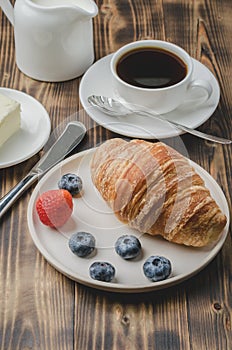 Delicious breakfast with fresh berries. Coffee cup, creamer and croissant with berries in white bowl and butter on wooden
