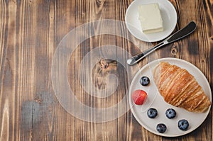 Delicious breakfast with fresh berries. Croissant with berries in white bowl and butter on wooden table. Copy space and copyspace