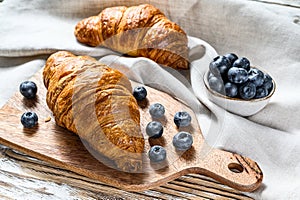Delicious breakfast with fresh croissants and blueberries. White wooden background. Top view