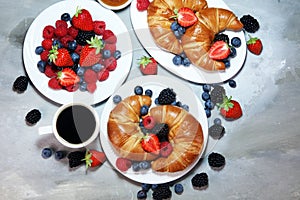 Delicious breakfast with fresh croissants and ripe berries on old marble background.