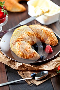 Delicious breakfast with fresh croissants and ripe berries on old wooden background