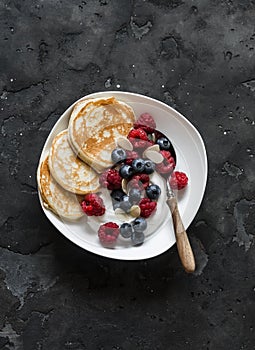 Delicious breakfast - Greek yogurt with berries and mini pancakes on a dark background, top view