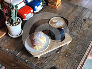 Delicious Breakfast; Heart love Latte art coffee in Black cup and Croissant topped with icing sugar