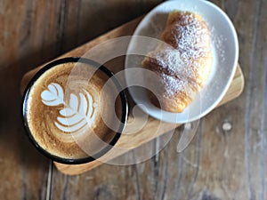 Delicious Breakfast; Heart love Latte art coffee in Black cup and Croissant topped with icing sugar