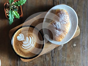 Delicious Breakfast; Heart love Latte art coffee in Black cup and Croissant topped with icing sugar