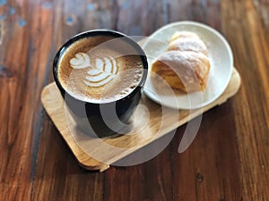 Delicious Breakfast; Heart love Latte art coffee in Black cup and Croissant topped with icing sugar