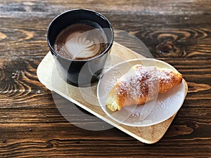 Delicious Breakfast; Heart love Latte art coffee in Black cup and Croissant topped with icing sugar