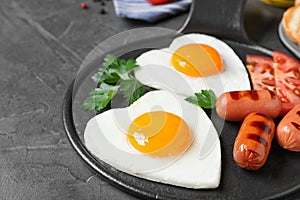 Delicious breakfast with heart shaped fried eggs and sausages on dark grey table