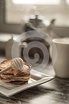 Delicious breakfast. Homemade Pancakes with honey and cup of tea on wooden rustic background table. Vintage style retro toned imag