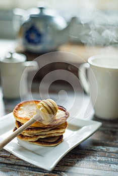 Delicious breakfast. Homemade Pancakes with honey and cup of tea on wooden rustic background table. Vintage style retro toned imag