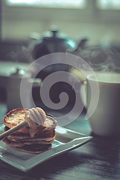 Delicious breakfast. Homemade Pancakes with honey and cup of tea on wooden rustic background table. Vintage style retro toned imag