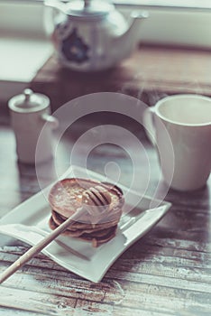 Delicious breakfast. Homemade Pancakes with honey and cup of tea on wooden rustic background table. Vintage style retro toned imag