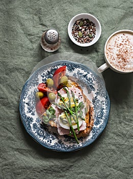 Delicious breakfast - sandwich with boiled egg, ham, asparagus, tomatoes, olives and cappuccino on the table, top view