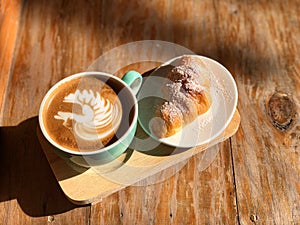 Delicious Breakfast; swan shape Latte art coffee in Green and white cup and Croissant topped with icing sugar