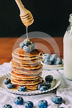 Delicious breakfast Sweet homemade stack of Oat pancakes with berries, honey, maple syrup, and milk bottle on wooden