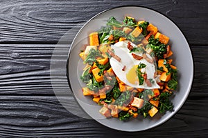 Delicious breakfast of sweet potato with kale, bacon and fried egg close-up on a plate. horizontal top view