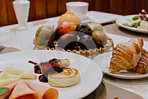Delicious breakfast with syrniki, ham, cheese, croissants, and fruits