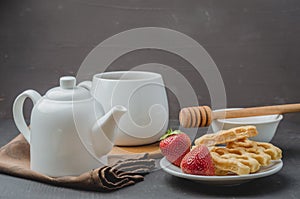 Delicious breakfast with tea, honey and wafers decorated with fresh strawberry on a stone table. Selective focus