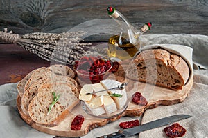 Delicious brie cheese Camembert with sun-dried tomatoes with olive oil and homemade bread. Traditional quick snack for home