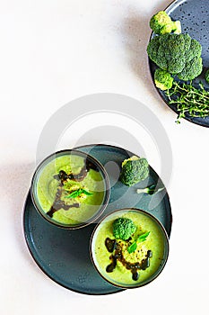 Delicious broccoli cream soup served with spicy oil and mint. Vegetarian dish. Top view. Light concrete background