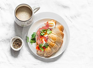 Delicious brunch, breakfast - coffee with cream and croissant sandwich with cream cheese, salmon and boiled egg on a light