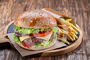 Delicious burger with  potato fries on a wooden table with a dark brown background behind. Fast food concept