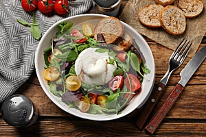 Delicious burrata salad with colorful cherry tomatoes, croutons and arugula served on wooden table, flat lay