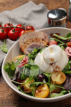 Delicious burrata salad with colorful cherry tomatoes, croutons and arugula on wooden table, closeup