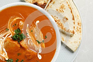 Delicious butter chicken in bowl and naan on table, top view.