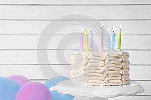 Delicious cake with burning candles and festive decor near wall. Space for text