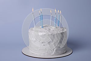 Delicious cake with cream and burning candles on light blue background