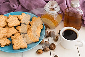 Delicious Canadian maple cream cookies on blue plate with honey, maple syrup, acorns and white cup of black coffee